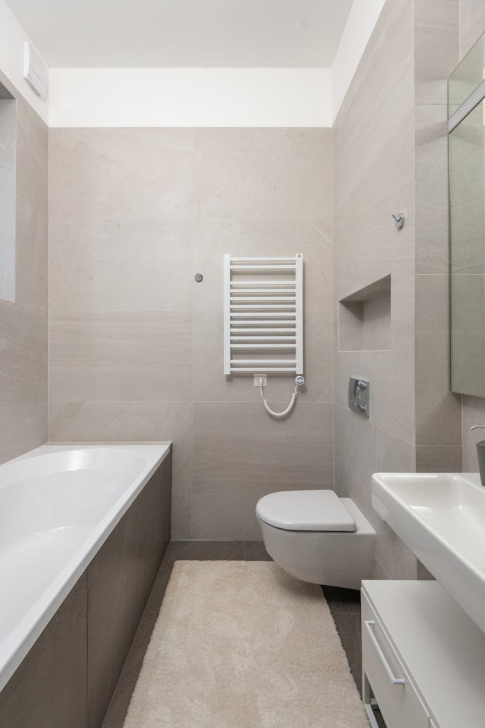 Ceramic bathtub with toilet bowl and sink in modern bathroom with beige tiled walls